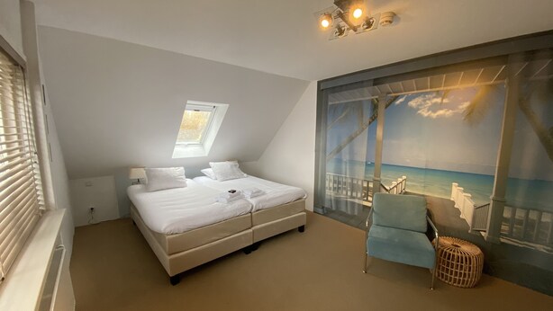 Une chambre à coucher comprenant un lit, une chaise, une fenêtre et une fresque murale représentant une scène de plage.
