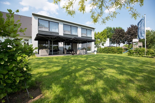 A modern hotel with a covered outdoor seating area, a well-maintained lawn, and a playground.