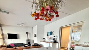 Une cuisine moderne avec des meubles blancs, un îlot central et une composition florale suspendue.