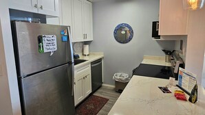 Una cocina compacta con armarios blancos, un refrigerador de acero inoxidable, un lavamanos y una encimera con una cafetera.