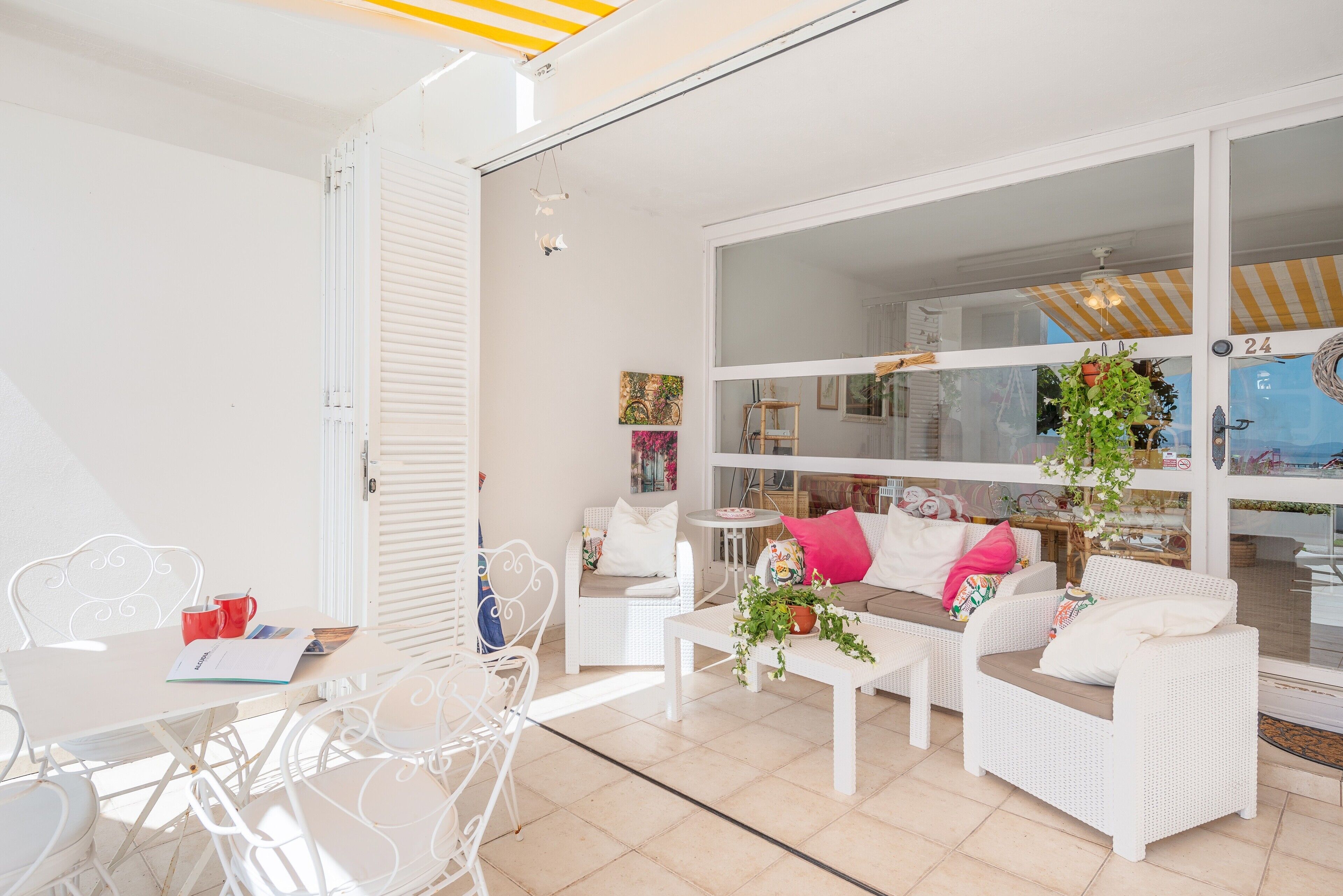 Un espace de vie lumineux et décloisonné, avec des meubles en osier blancs, une porte vitrée donnant sur un balcon et une petite table sur laquelle est posée une tasse rouge.