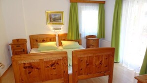 A room with two wooden beds, a bedside table, a nightstand, and a window with green curtains. - Pepi's vacation apartments including summer card with   17 services (Jerzens)