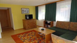 A living room with a sofa, a television on a wooden cabinet, a patterned rug, and a door leading to another room. - Pepi's vacation apartments including summer card with   17 services (Jerzens)