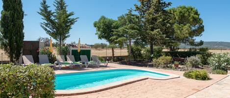 A swimming pool with lounge chairs, surrounded by trees and a clear sky.