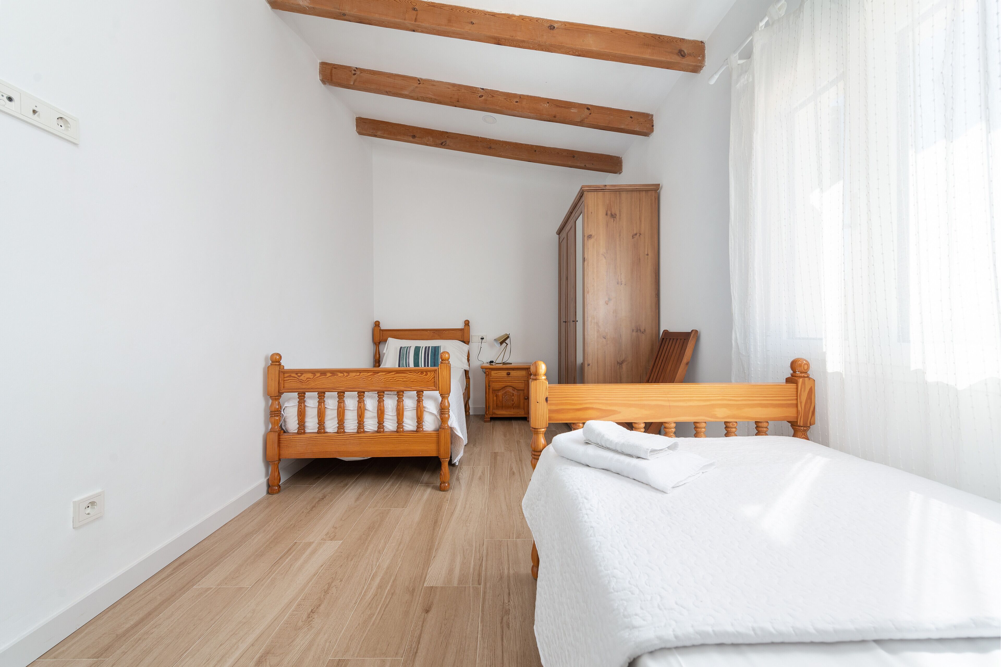A bedroom with two wooden beds, a wardrobe, and a nightstand.