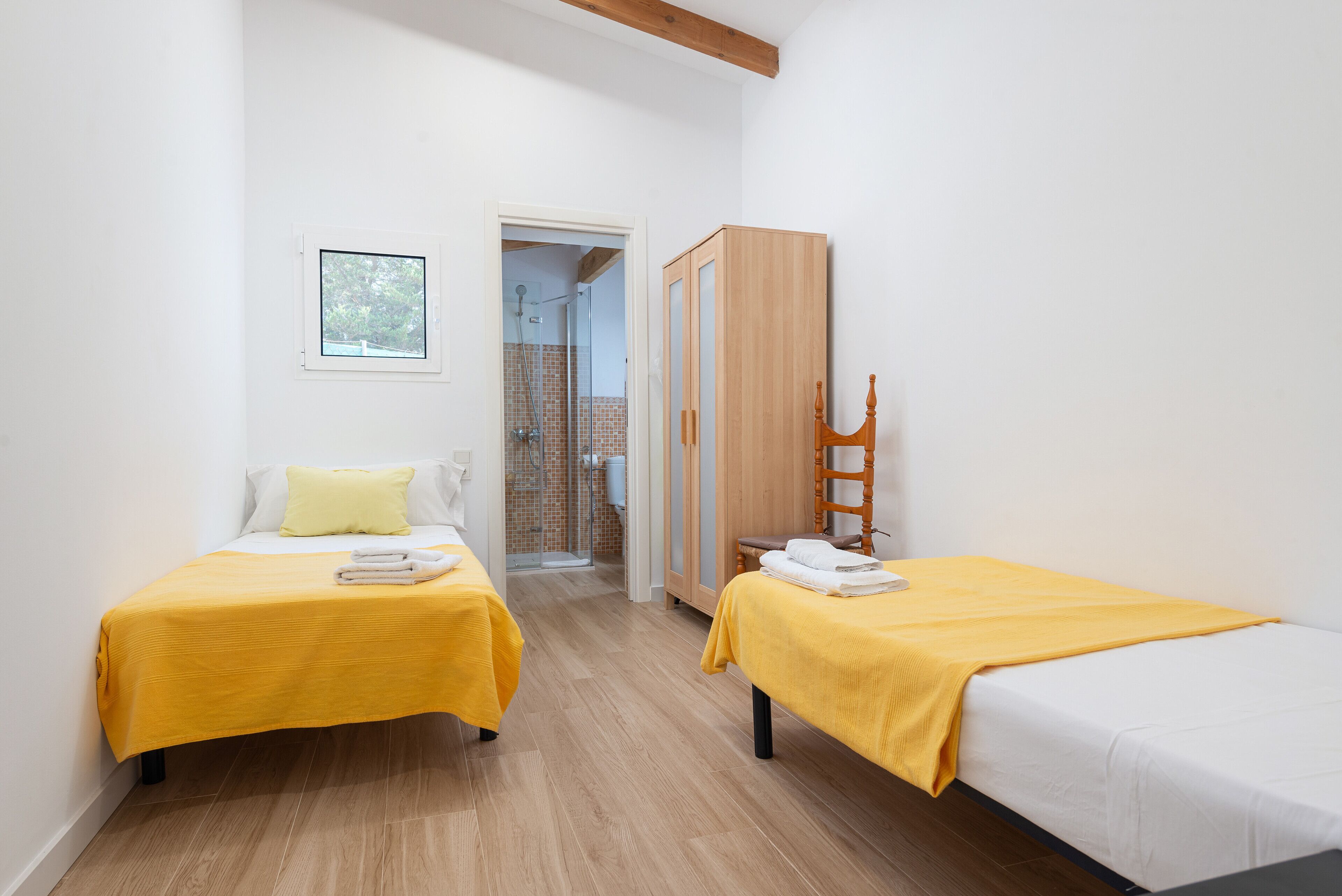 A bedroom with two beds, a wooden wardrobe, and a shower area.