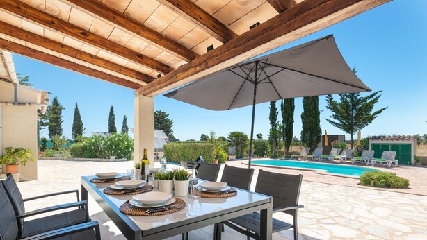 An outdoor patio with a table set for dining, surrounded by chairs, and an umbrella providing shade. - CA NA MENUDA - Cosy country house with private pool in quiet surroundings. Free WiFi (Sencelles)