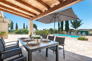 Een terras buiten met een eettafel, omringd door stoelen, en een parasol voor de schaduw.