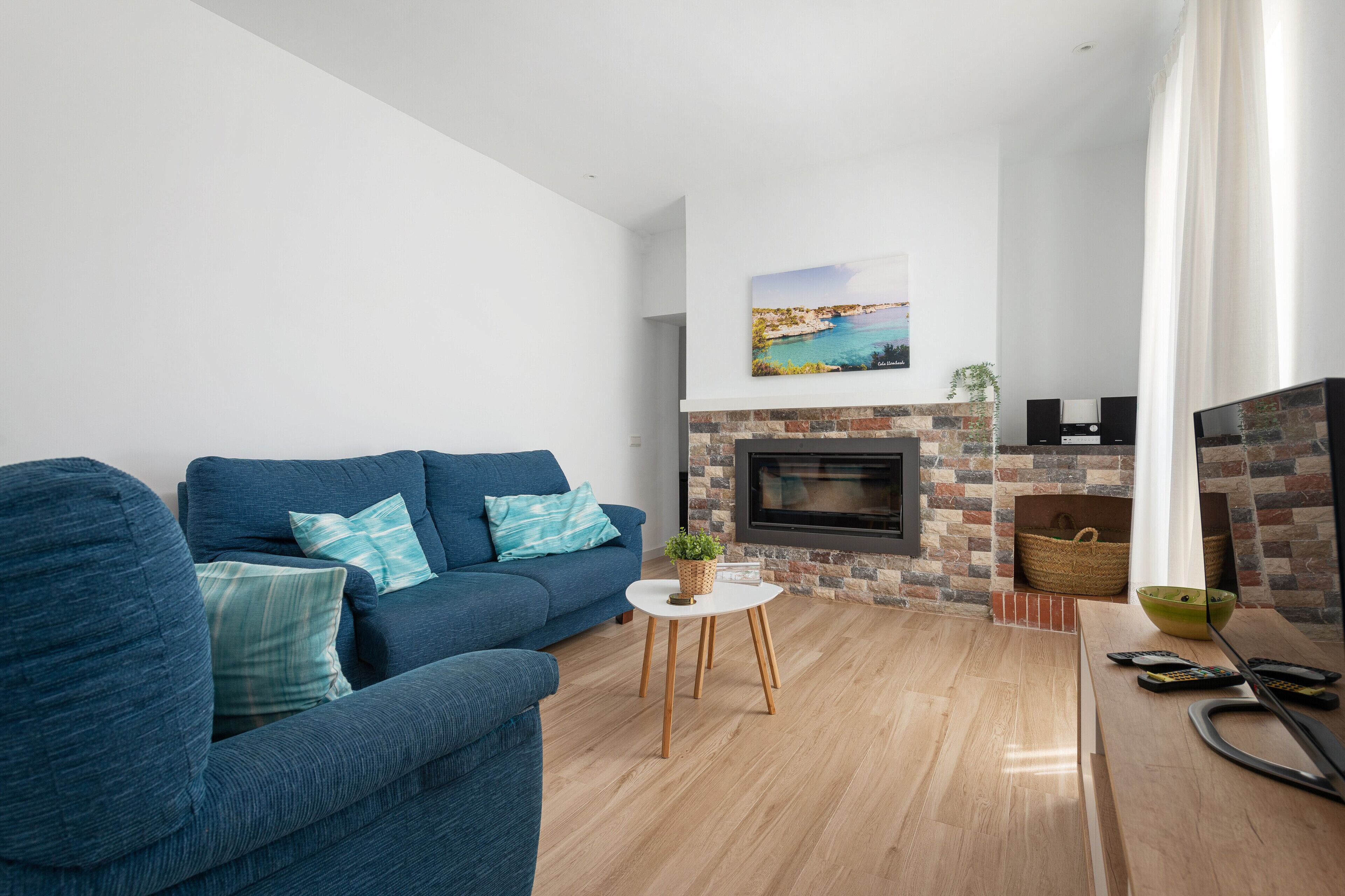 A living room with a blue sofa, a fireplace, and a view of the sea.