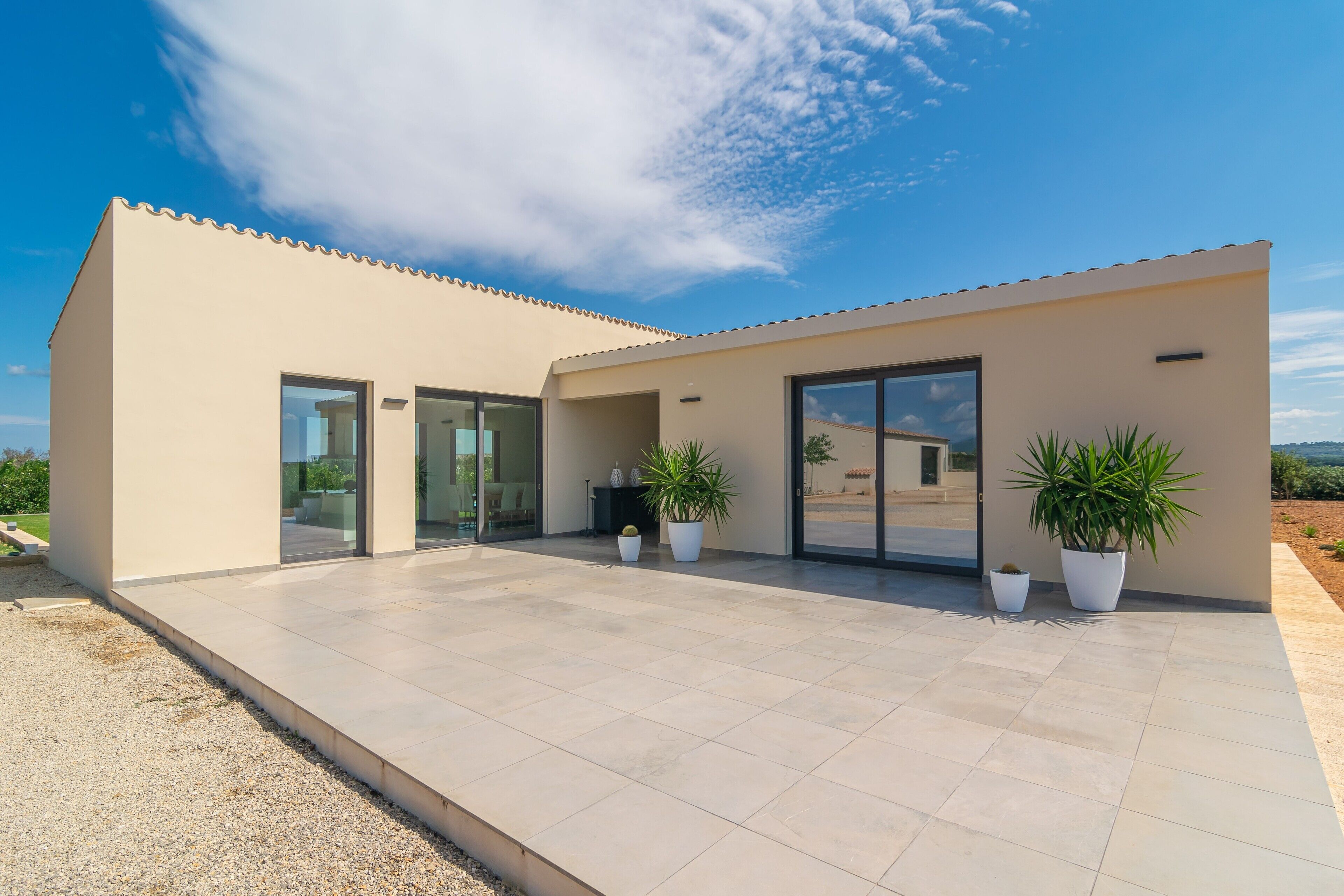 Una casa moderna con techo plano, puertas de cristal amplias y plantas en macetas.