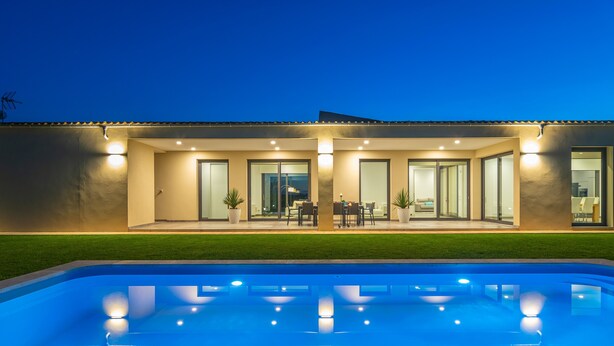 Una casa moderna con piscina, ventanas amplias y mobiliario exterior.