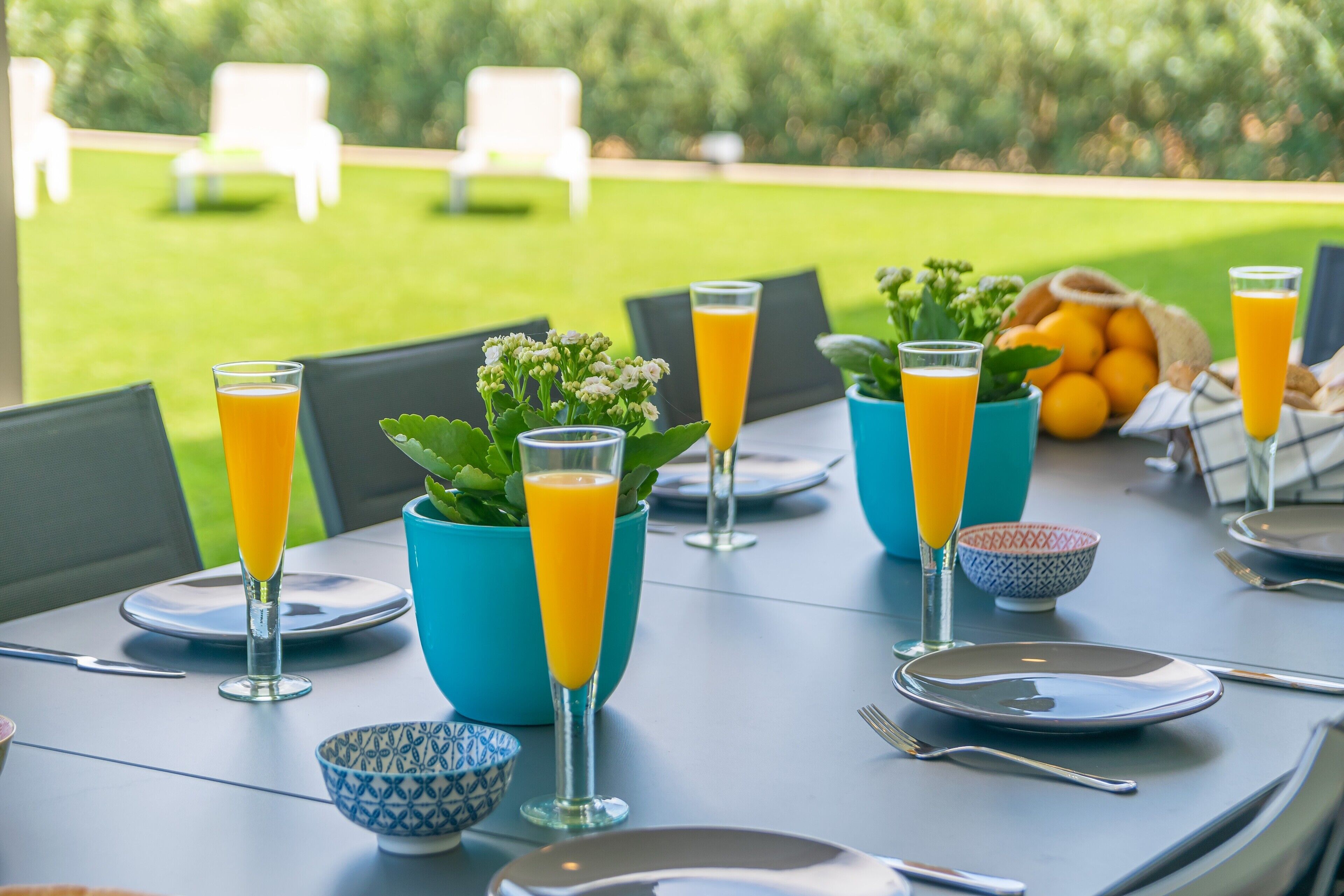 A table set for breakfast with orange juice, bowls, and plates, overlooking a garden.