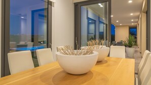 Un comedor moderno con una mesa de madera, sillas blancas y dos cuencos blancos con ramas decorativas.