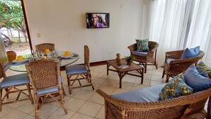 Ein Essbereich mit Korbmöbeln, einem runden Tisch und einem an der Wand befestigten Fernseher.