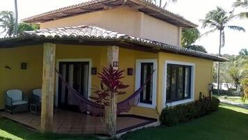 Relax on the covered porch with a hammock and two chairs amidst lush greenery and palm trees.