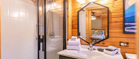 Une salle de bain avec une douche à parois de verre, un lavabo blanc avec un miroir au-dessus, et des murs recouverts de lambris en bois.