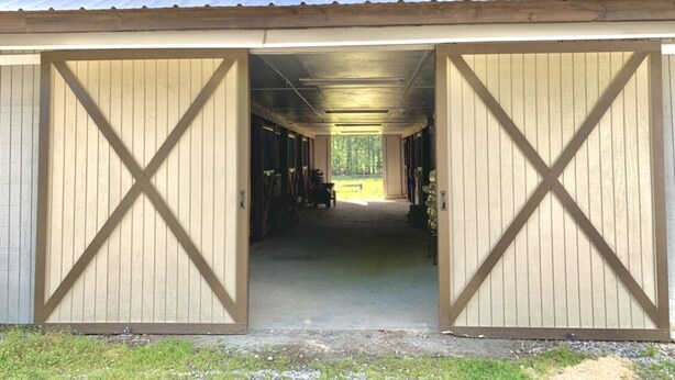 A barn with open doors revealing a long, narrow interior with wooden walls and a central aisle. - Regal Ranch Retreat *DOG & HORSE FRIENDLY* (Oxford)