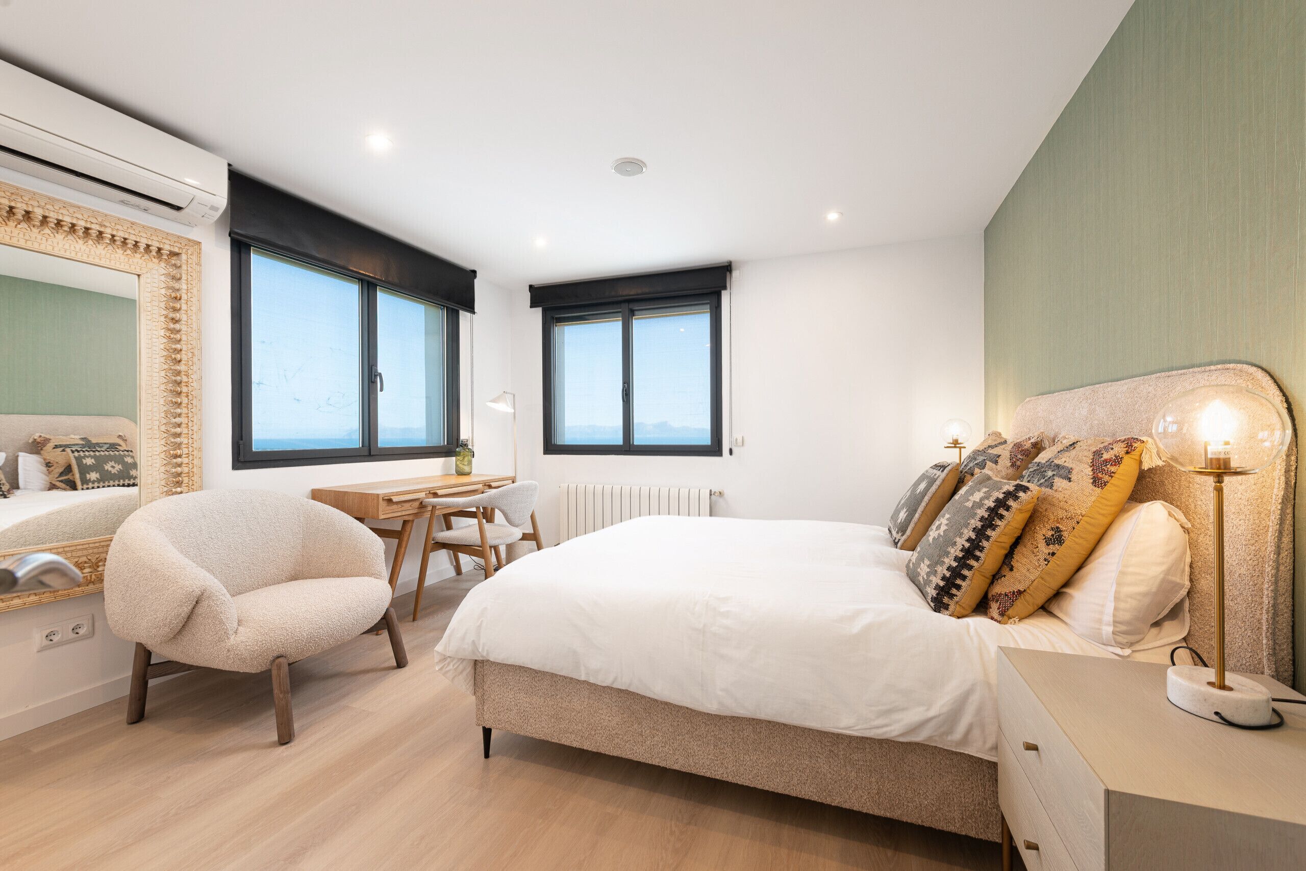 A modern bedroom with a bed, a chair, a desk, and a window.