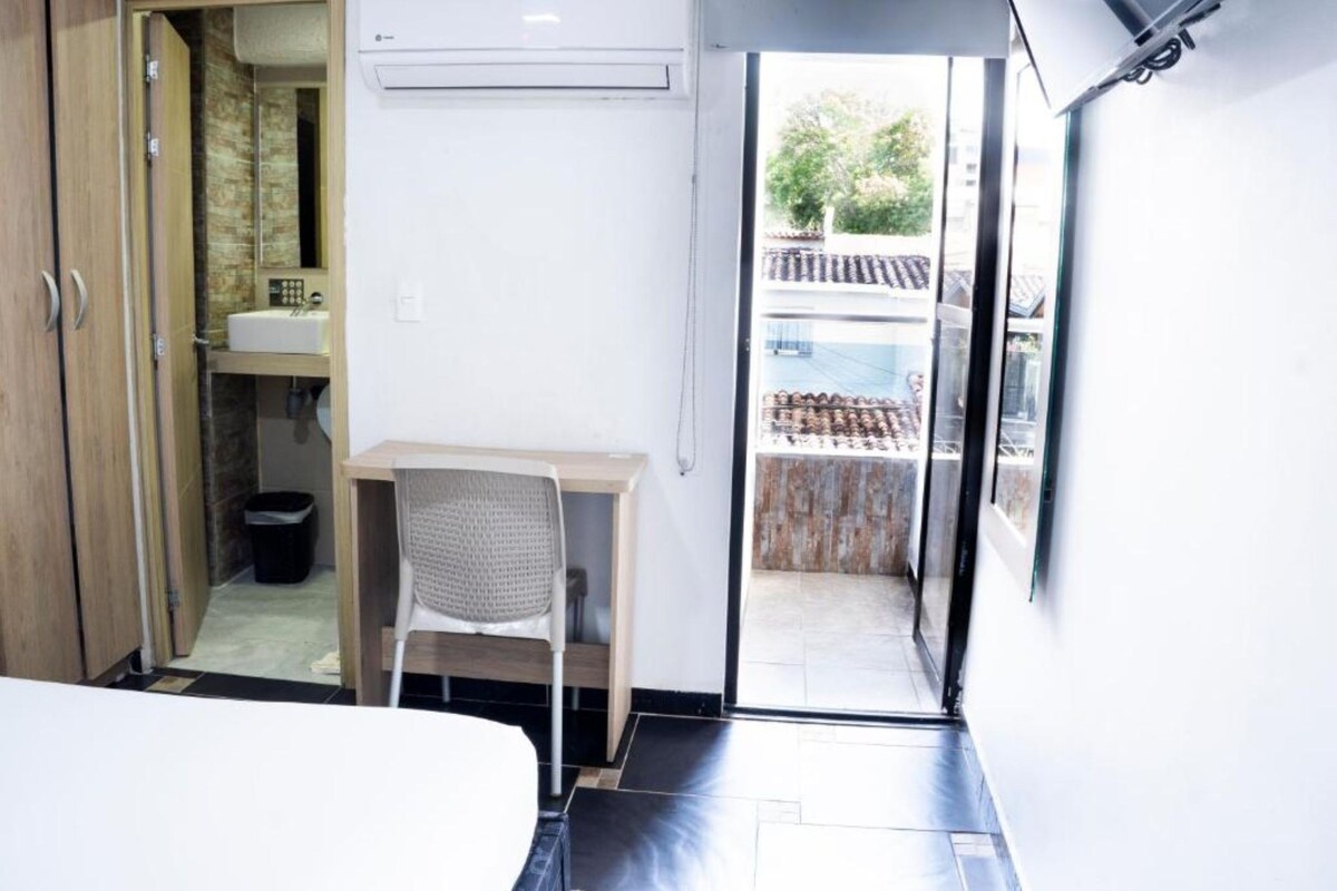 A compact room with a bed, a small desk, a chair, and a bathroom with a sink and toilet.