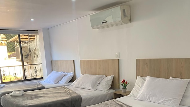 Habitación de hotel con dos camas, cada una con cabecero de madera, ropa de cama blanca y manta gris. Hay una ventana con vistas al exterior y un equipo de aire acondicionado en la pared.