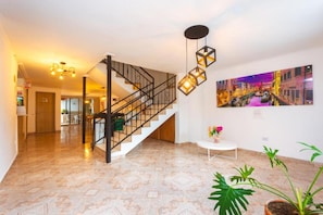 A spacious lobby with a staircase, a painting of a cityscape, and potted plants. - HOTEL COLORES BOUTIQUE    (Medellín)