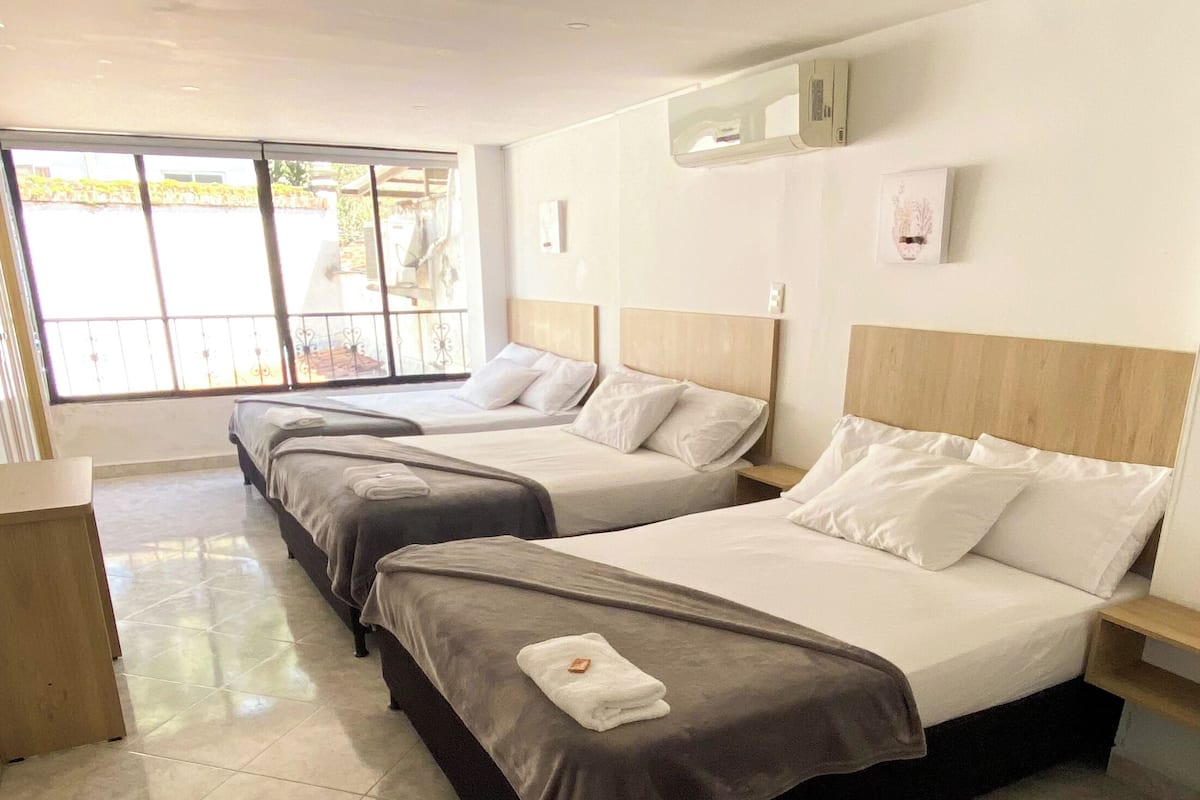 A hotel room with three beds, a large window, and a tiled floor.