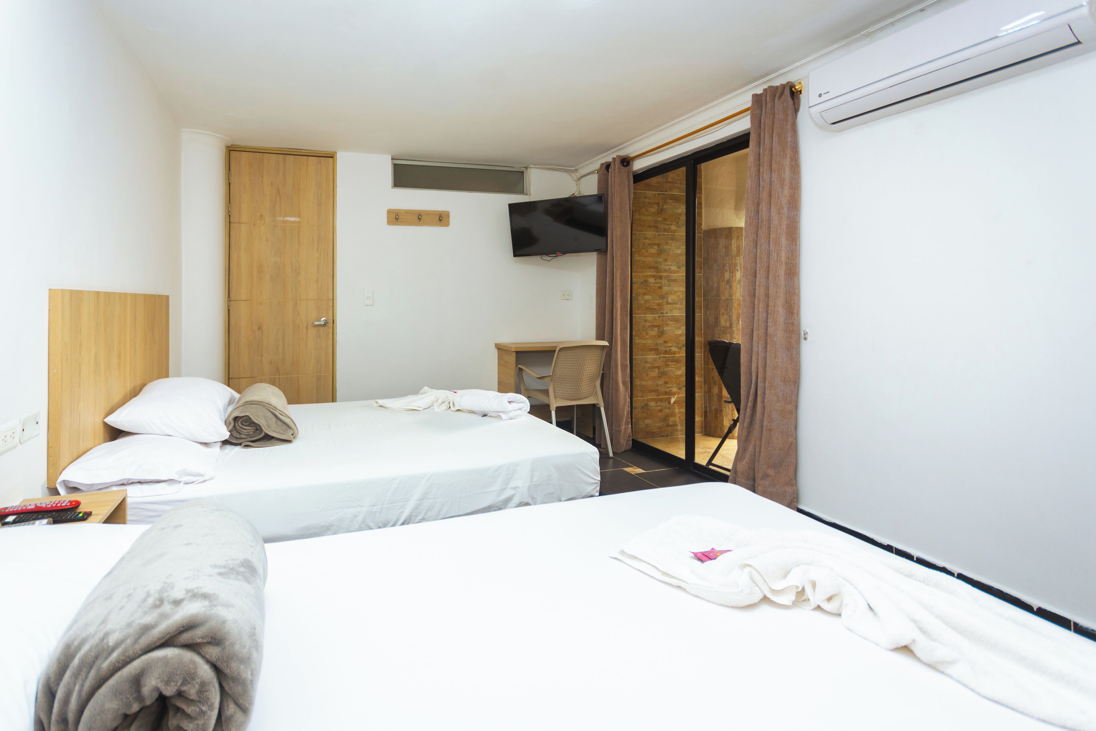 Quarto de hotel com duas camas, uma mesa, uma televisão e um ar condicionado.