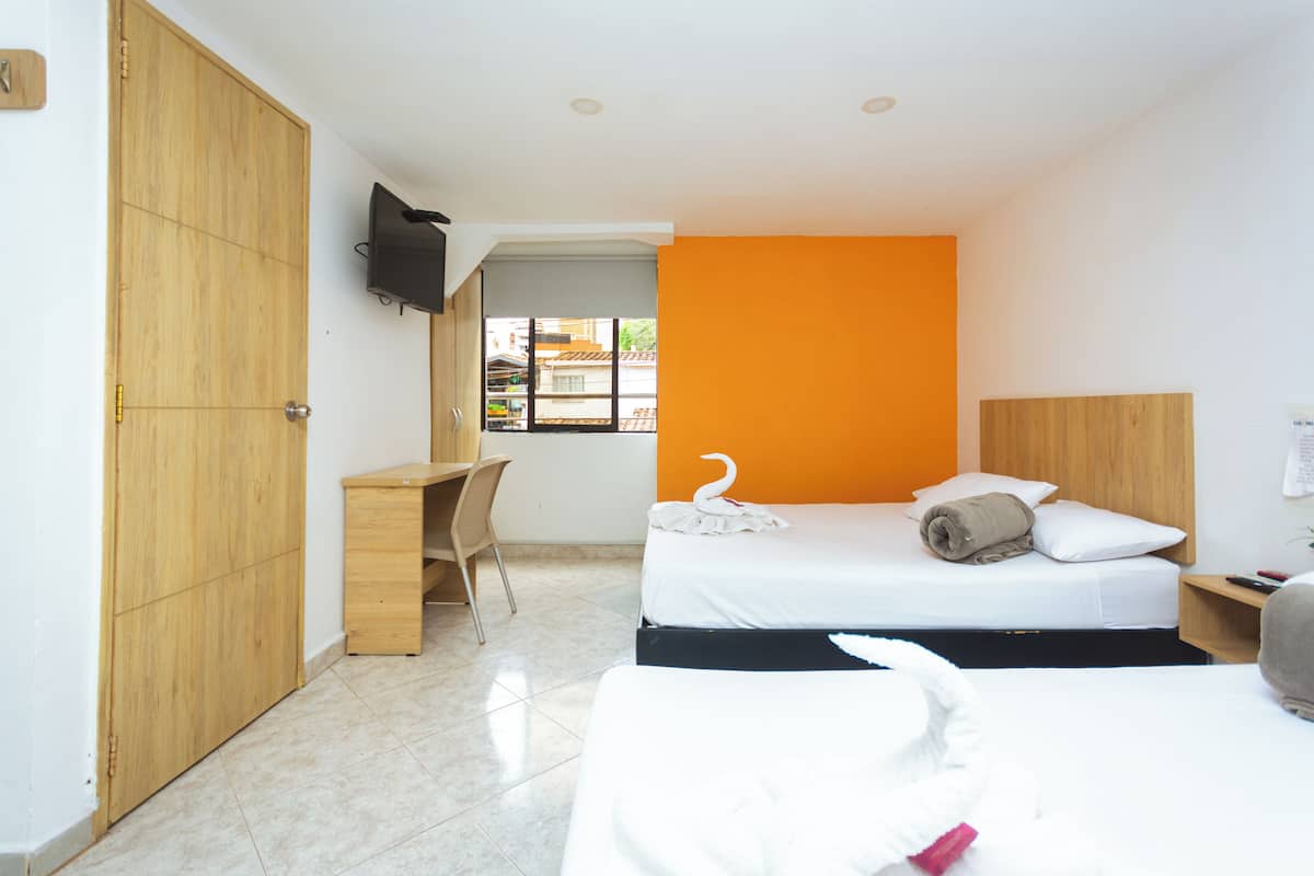 A hotel room with two beds, a desk, a TV, and a window with a view of the outside.