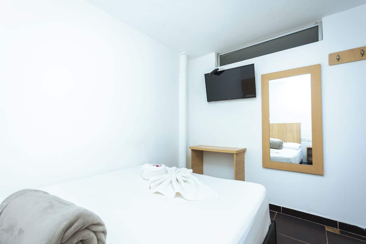 A hotel room with a bed, a TV mounted on the wall, a wooden nightstand, and a mirror.