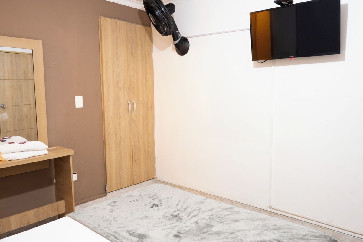 A bedroom with a wooden wardrobe, a marble floor, a wall-mounted TV, and a ceiling fan.