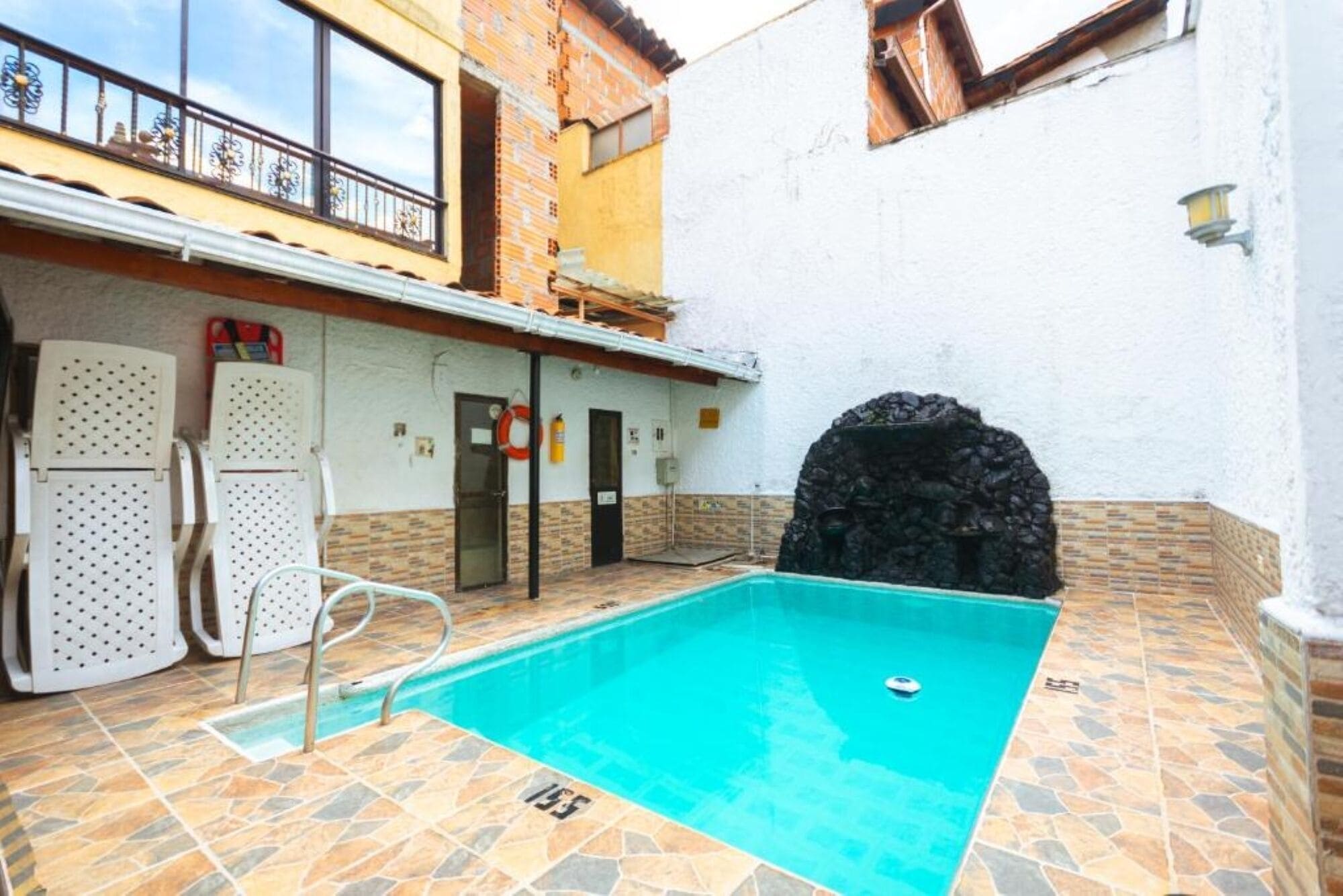Una piscina con pared de piedra y una zona cubierta con sillas.