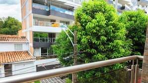Un edificio de varios pisos con balcones, un coche rojo estacionado abajo y un árbol verde al frente.