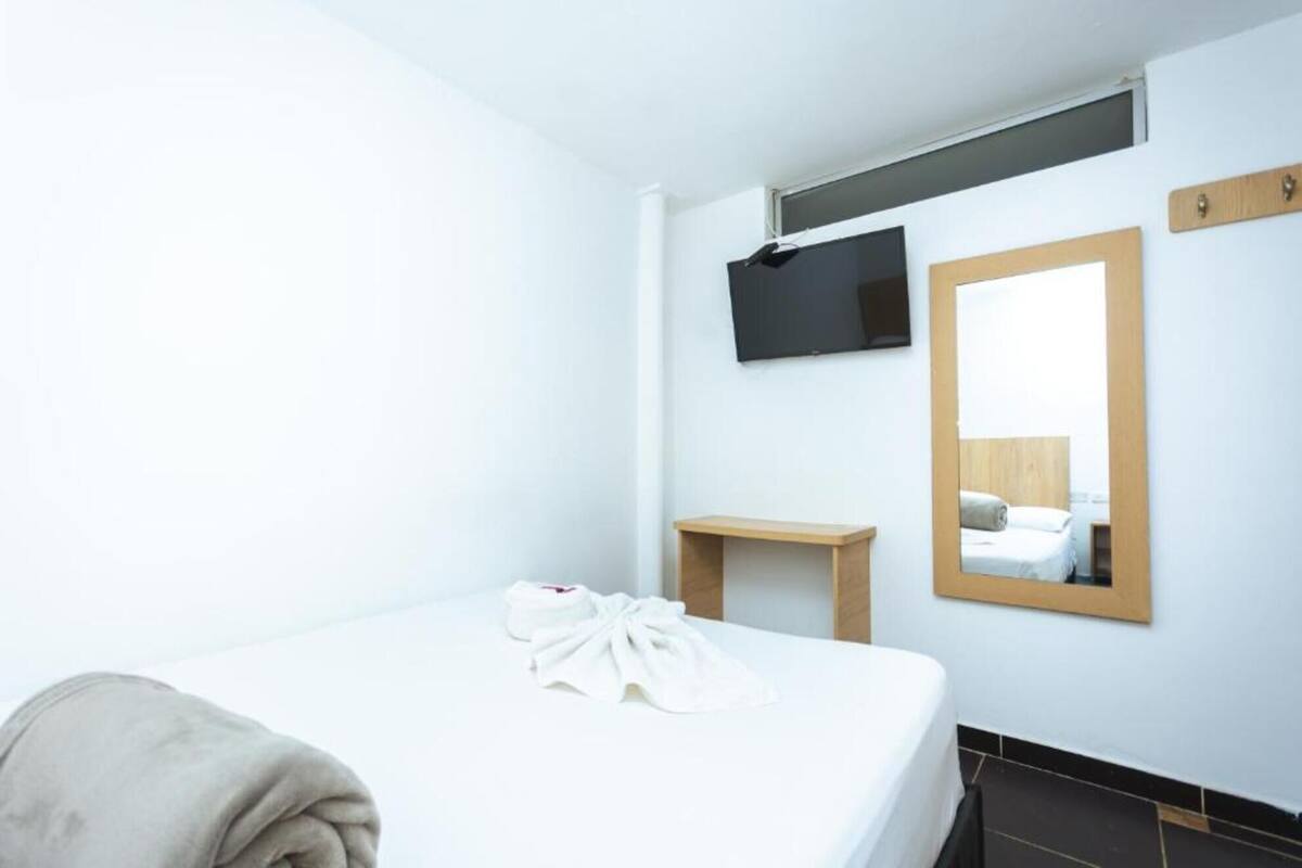 A hotel room with a bed, a bedside table, a TV mounted on the wall, and a mirror.