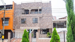 Un edificio moderno de dos pisos con fachada de piedra, entrada protegida por una reja y un camino de entrada con baldosas a cuadros.