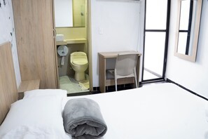 A hotel room with a bed, a desk, a chair, a toilet, and a mirror. - HOTEL COLORES BOUTIQUE    (Medellín)