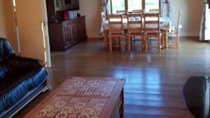 Un salón amplio con piso de madera, un sofá, una mesa de centro, una mesa de comedor con sillas y un aparador.