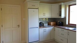 Una cocina con armarios blancos, un refrigerador, una cafetera y un ventanal.