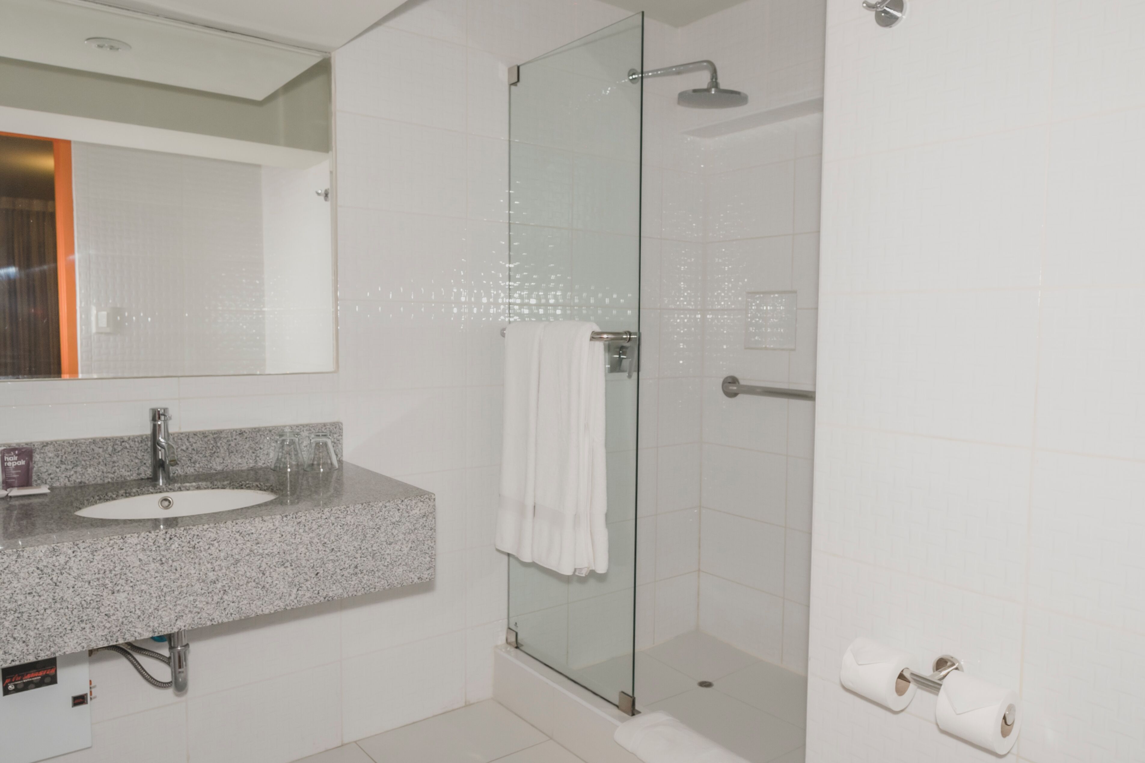 A modern bathroom with a granite countertop sink, a glass shower enclosure, and a white towel hanging on the door.