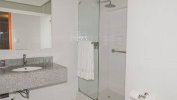 A modern bathroom with a granite countertop sink, a glass shower enclosure, and a white towel hanging on the door.