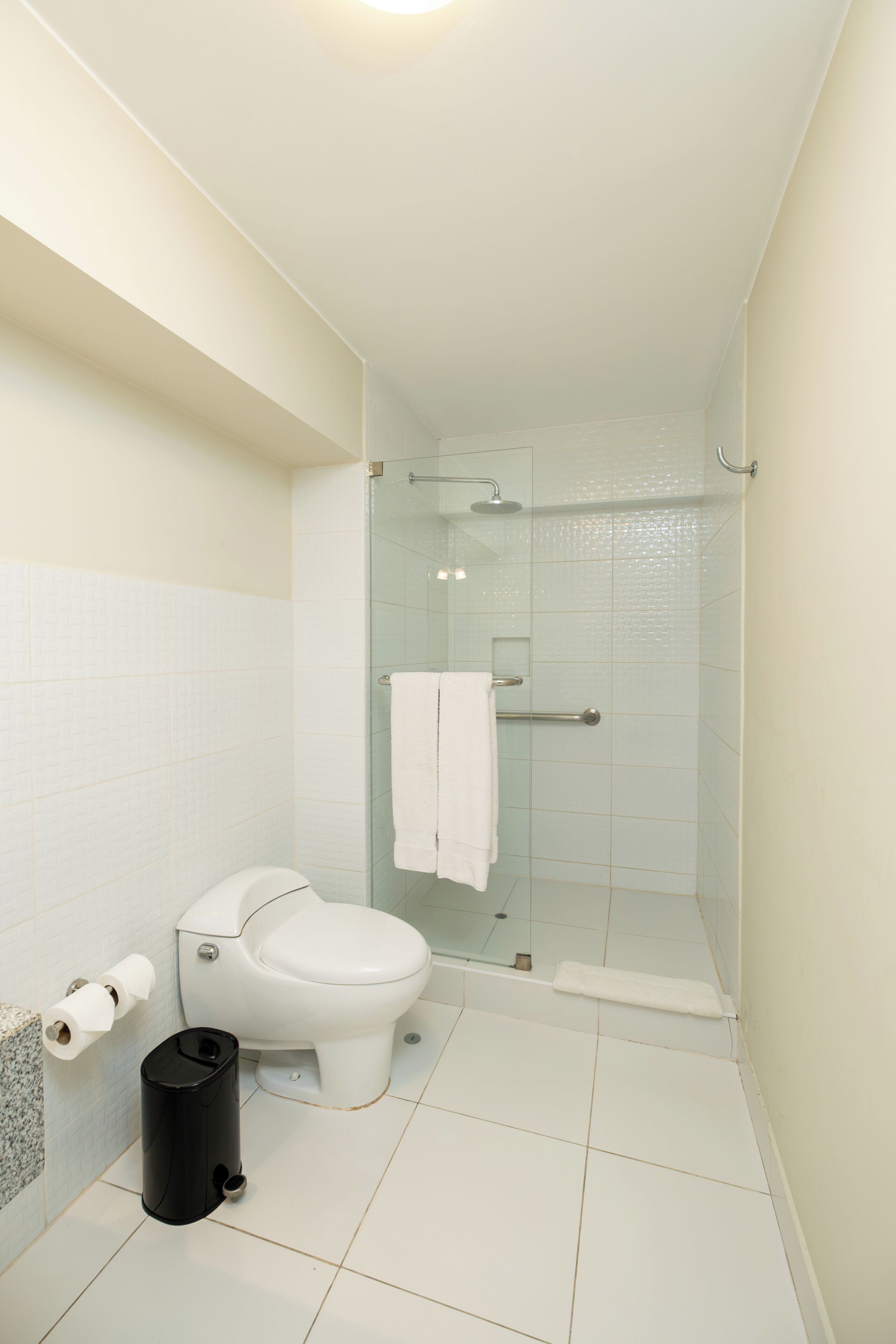 Een badkamer met toilet, een douchecabine van glas en een prullenbak.
