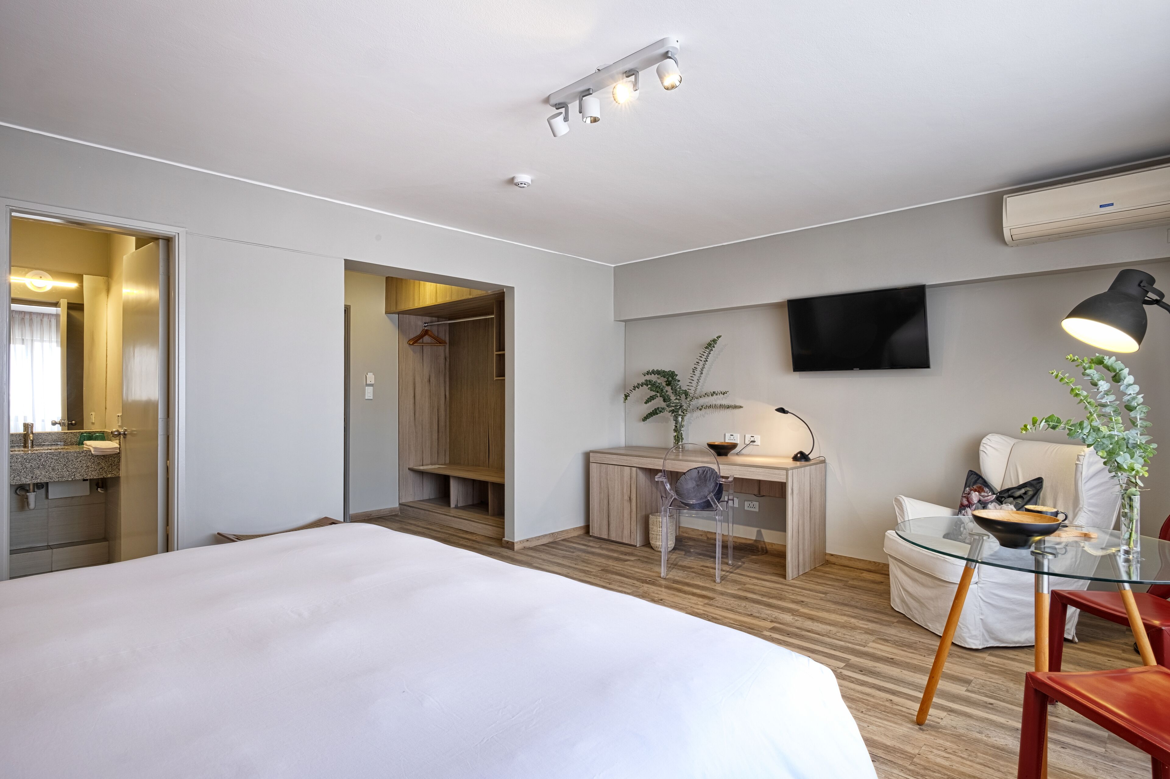 Et moderne hotelværelse med en stor seng, et skrivebord med stol, et fjernsyn og et glasbord med lampe.