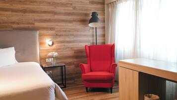 Un dormitorio con piso de madera, una cama, una silla roja, un escritorio y una lámpara.