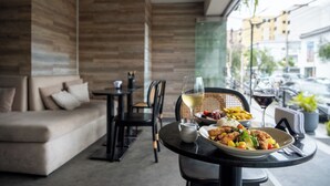 Un coin repas avec une table dressée pour deux personnes, un canapé et une fenêtre donnant sur la rue.
