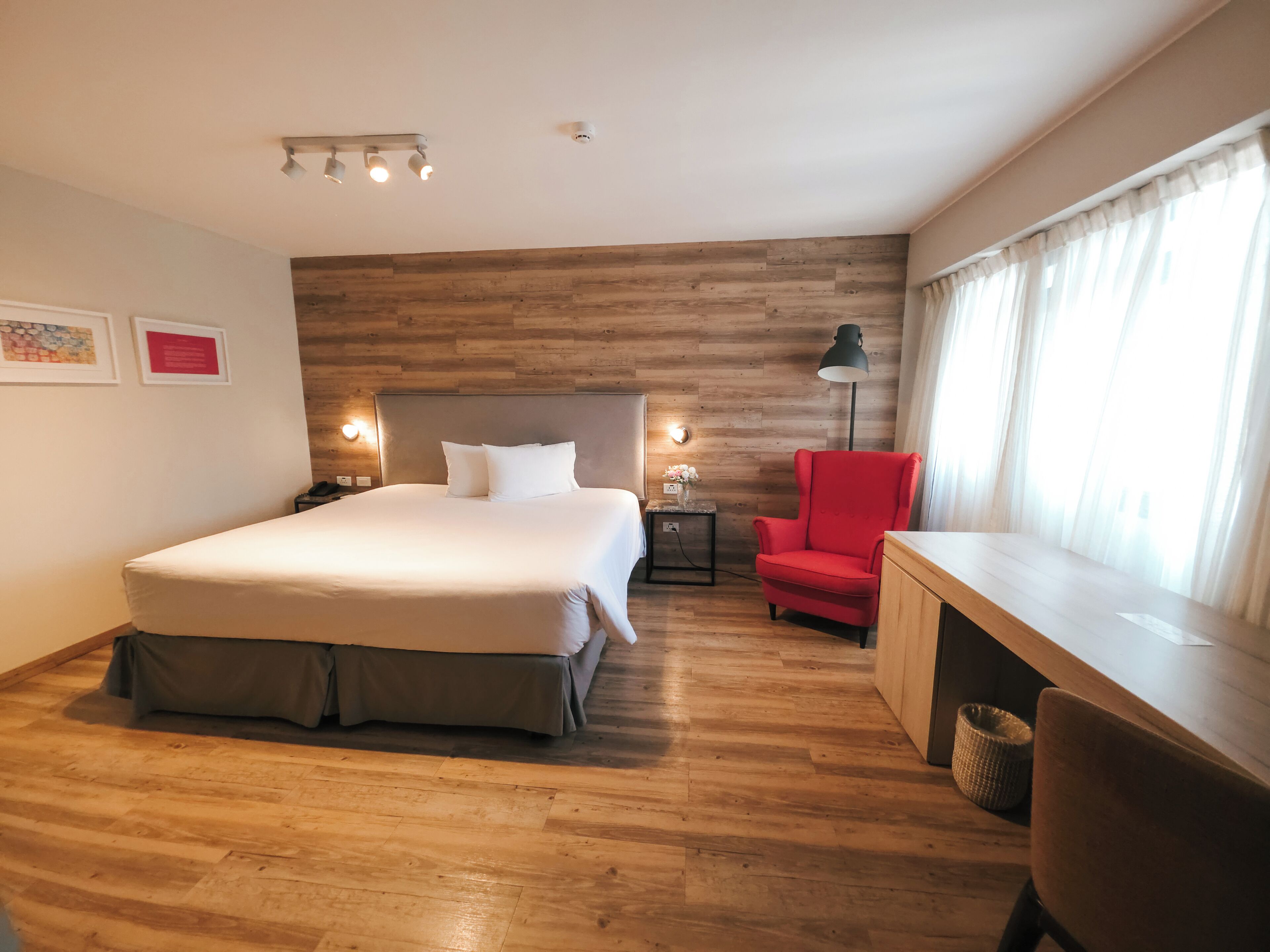 A hotel room with a large bed, a desk, a chair, and a nightstand.