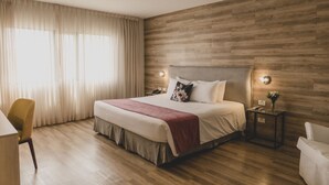 Une chambre d’hôtel moderne avec un mur en bois, un grand lit recouvert d’un plaid rouge, une table de chevet avec une lampe et une chaise.