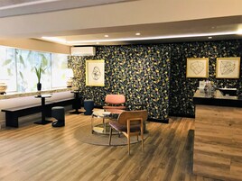 Una habitación de hotel moderna con suelo de madera, una mesa redonda de cristal, una silla acolchada, un banco, una pequeña mesa redonda, una planta en maceta y una pared con estampado floral.
