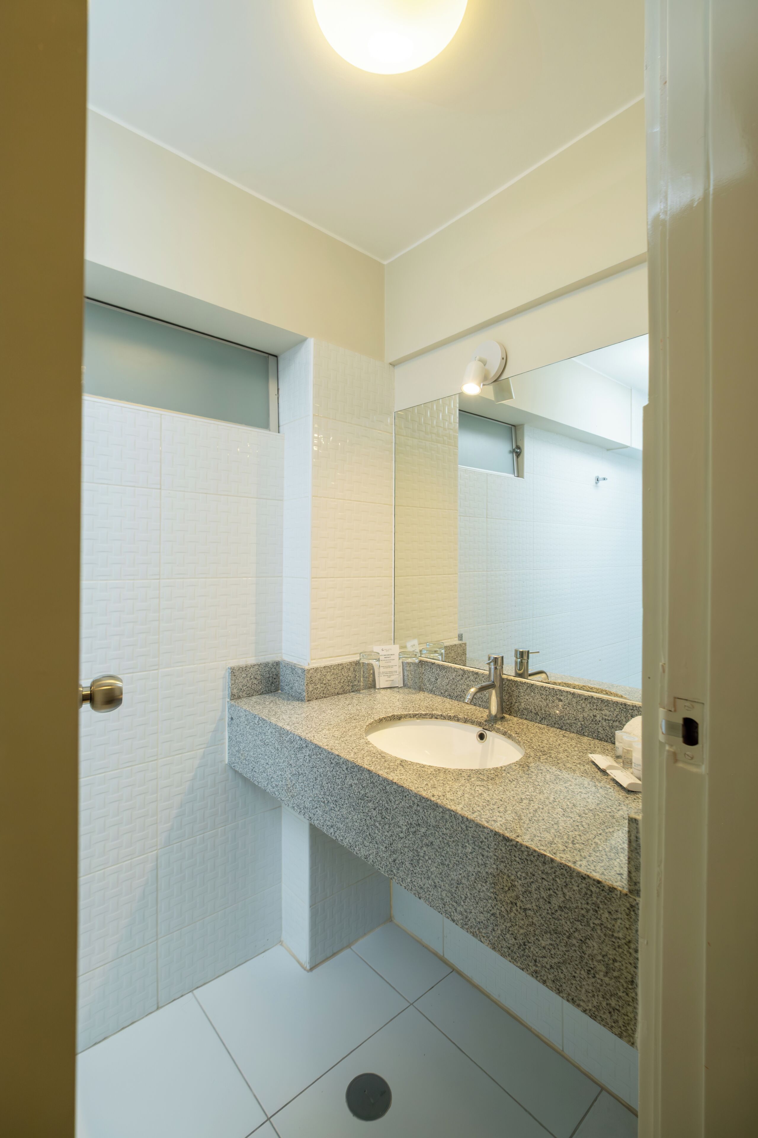 Un baño con lavamanos blanco, encimera de granito y espejo sobre el lavamanos.