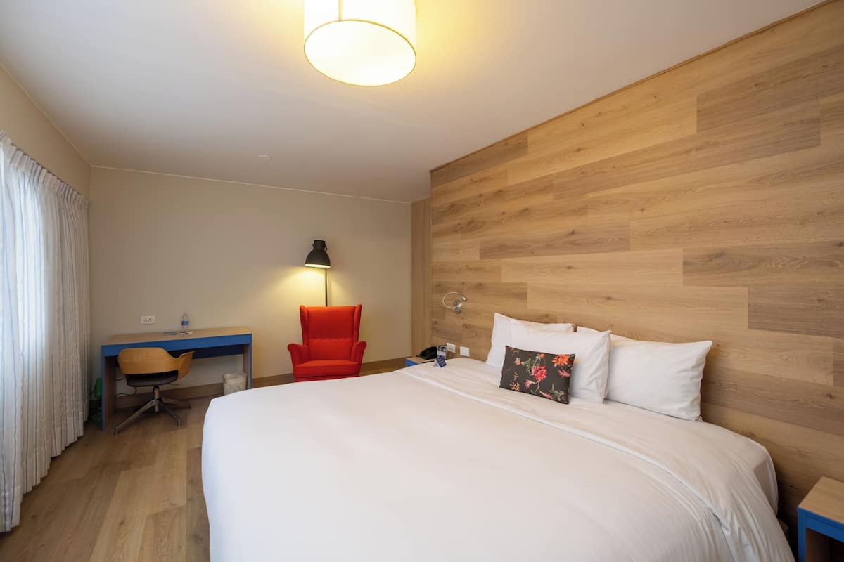 Una habitación de hotel con cama, escritorio, silla y lámpara.