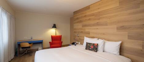 A hotel room with a bed, a desk, a chair, and a lamp.