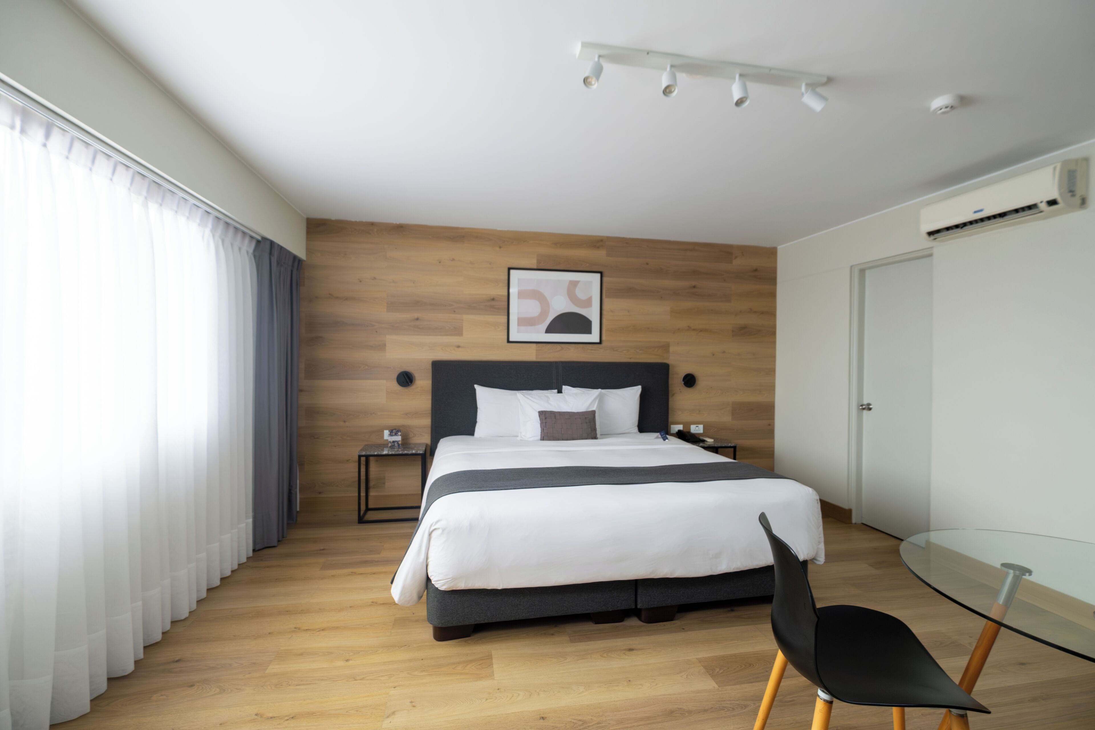 A modern hotel room with a large bed, a glass table, and a wooden floor.